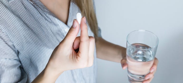 Woman holding a glass of water and a pill.