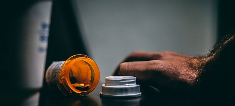 Spilled bottle of prescription pills next to a man's hand.