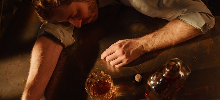 Man sleeping next to a bottle and glass of whiskey.